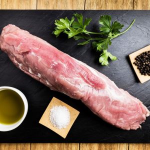 pork tenderloin with salt, black pepper, a bowl of oil and parsley on a black slate plate