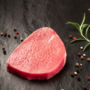 A photo of a steak of eye round beef, a raw cut, with rosemary, pepper and garlic on a black background with copy space